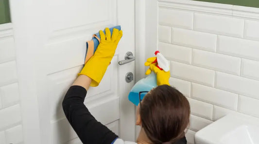 Professional bathroom deep cleaning service removing grime from door with spray and cloth. Expert limescale and bacteria removal for hygienic spaces.